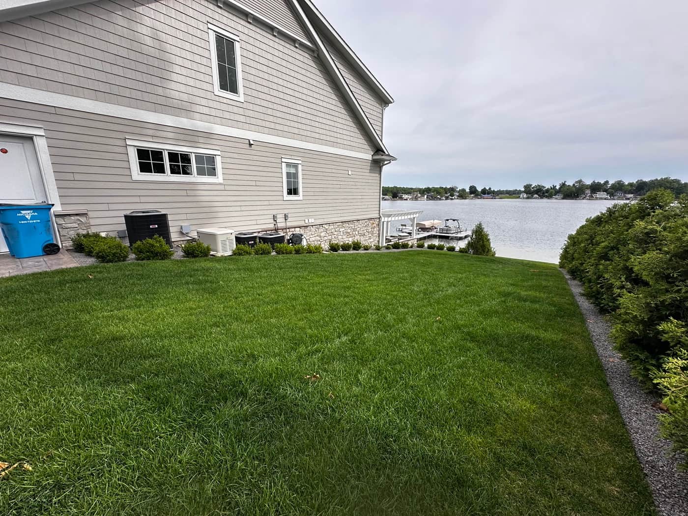 Lush green lawn beside a Southwest Michigan lakefront home with dock and arborvitae hedge