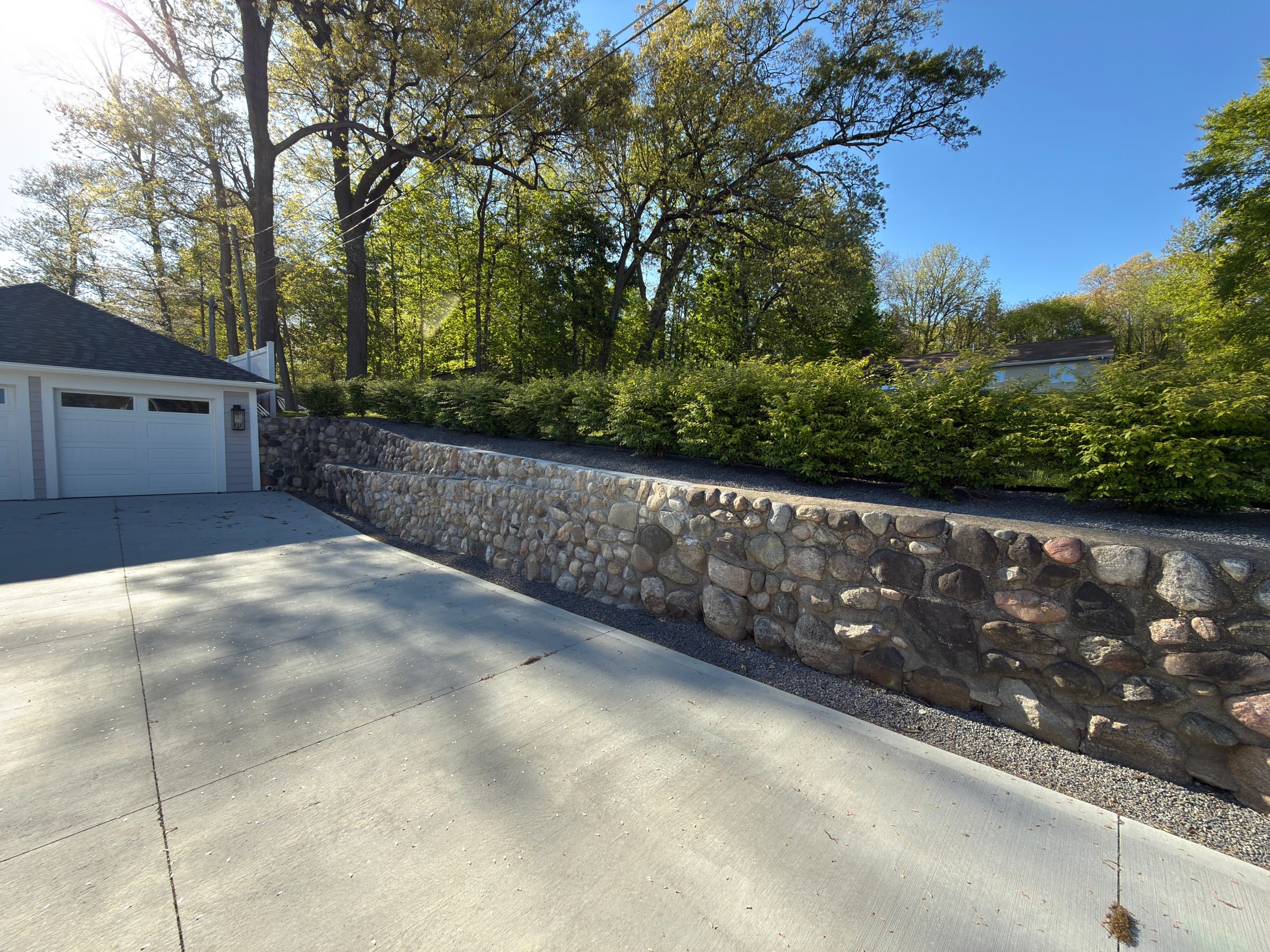 Natural boulder retaining wall alongside a clean concrete driveway, Southwest Michigan