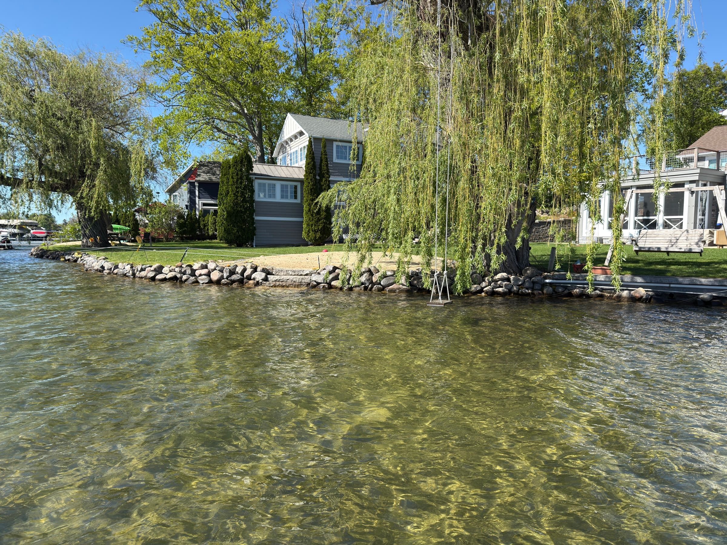 Stone shoreline stabilization with riprap edging along a Southwest Michigan lake, willow trees and clear water